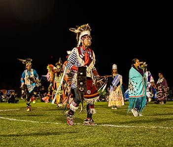 穿着传统印第安服装的舞者在夜间活动时在运动场上跳舞